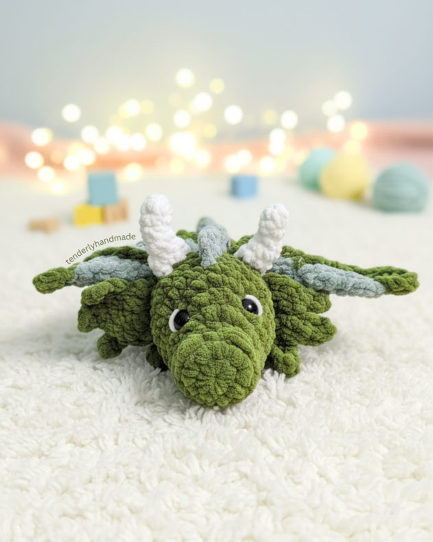 Frontal face view of a cute green crochet dragon with black safety eyes and white horns.