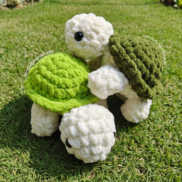 Overhead view of two soft crochet tortoise plushies with bright lime green and forest green shells side by side in the garden.