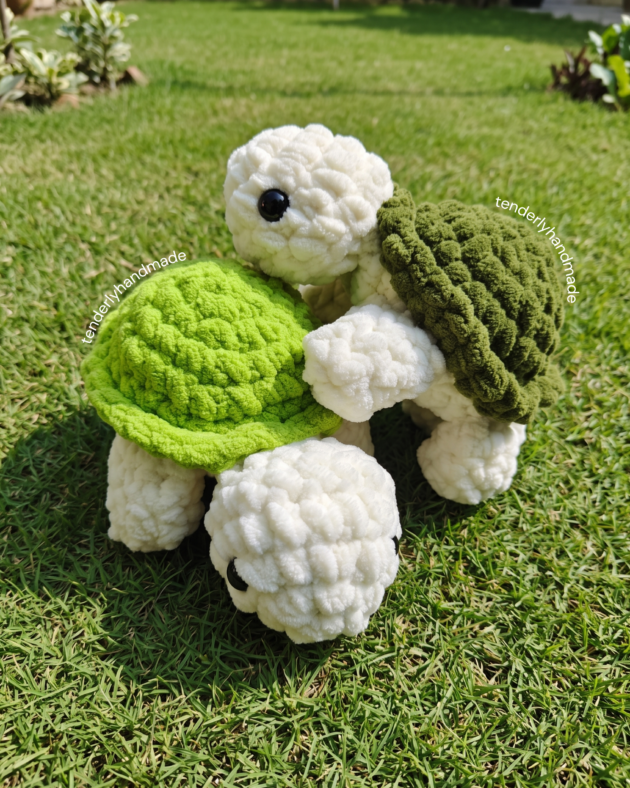 Overhead view of two soft crochet tortoise plushies with bright lime green and forest green shells side by side in the garden.