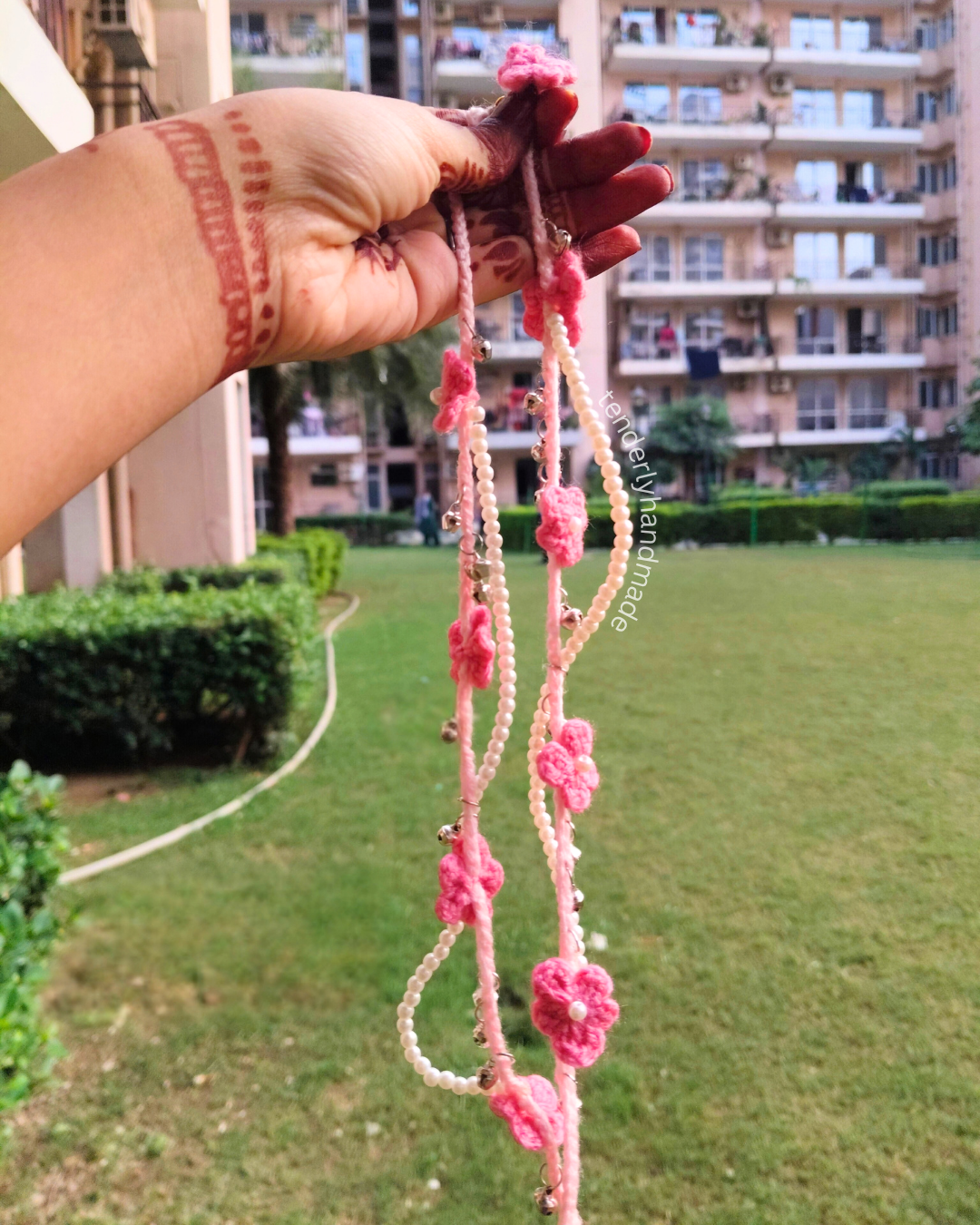 A hand holding the full length of two long pink crochet payals showing the 20 cm string length with floral drops and ghungroo accents.