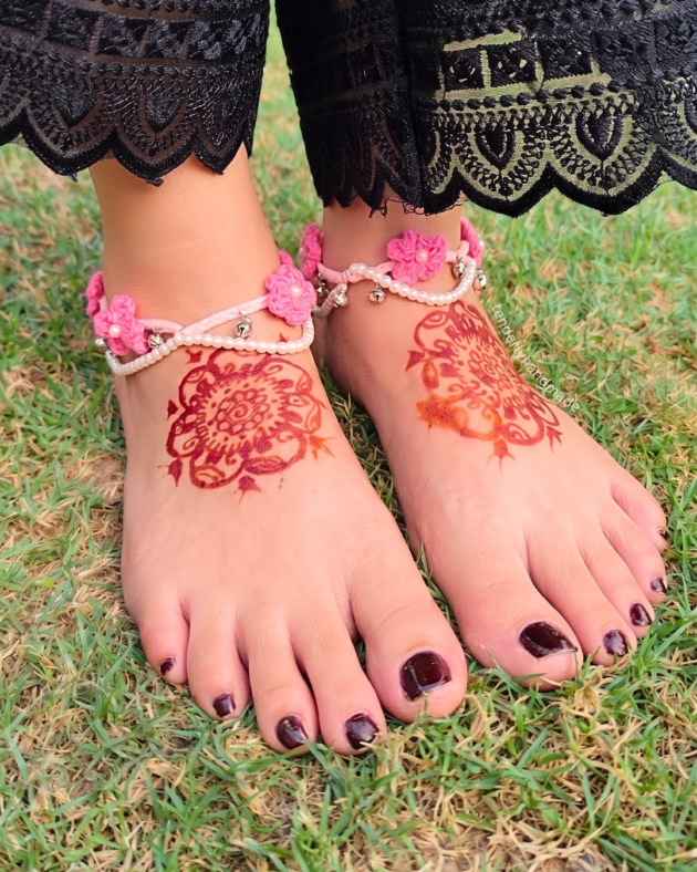Pair of pink handmade crochet payals with delicate flowers, pearl beads, and ghungroos worn on henna-decorated feet.