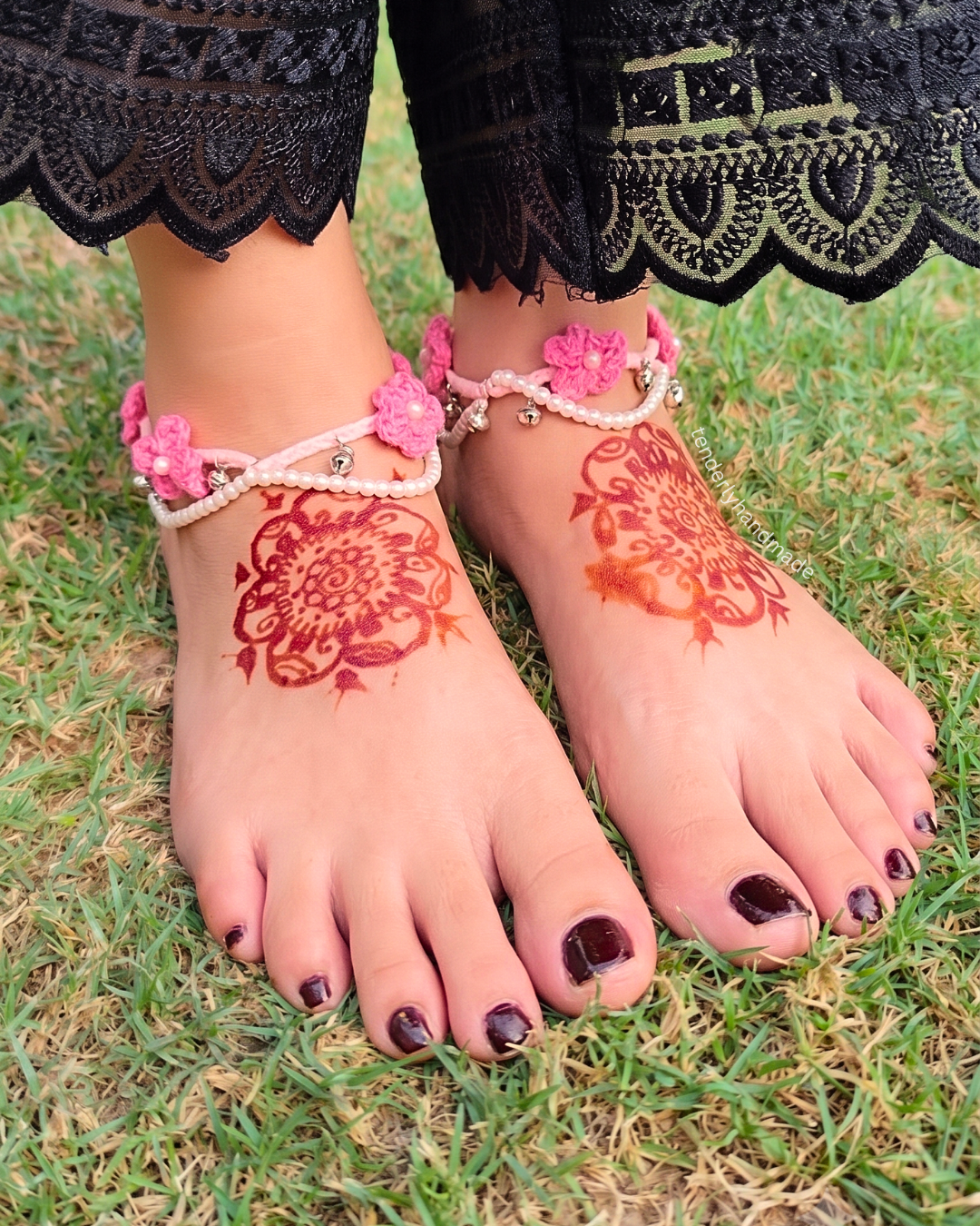 Pair of pink handmade crochet payals with delicate flowers, pearl beads, and ghungroos worn on henna-decorated feet.
