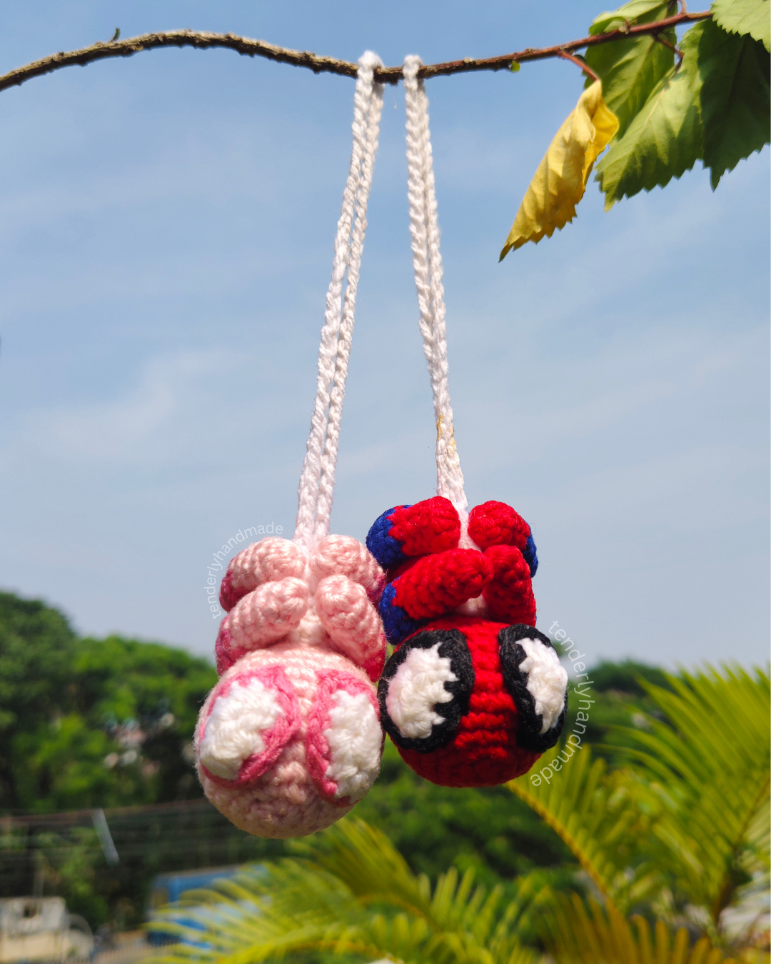 Spider-Man and Spider-Gwen crochet spiderman car hanging charms hanging side by side outdoors.